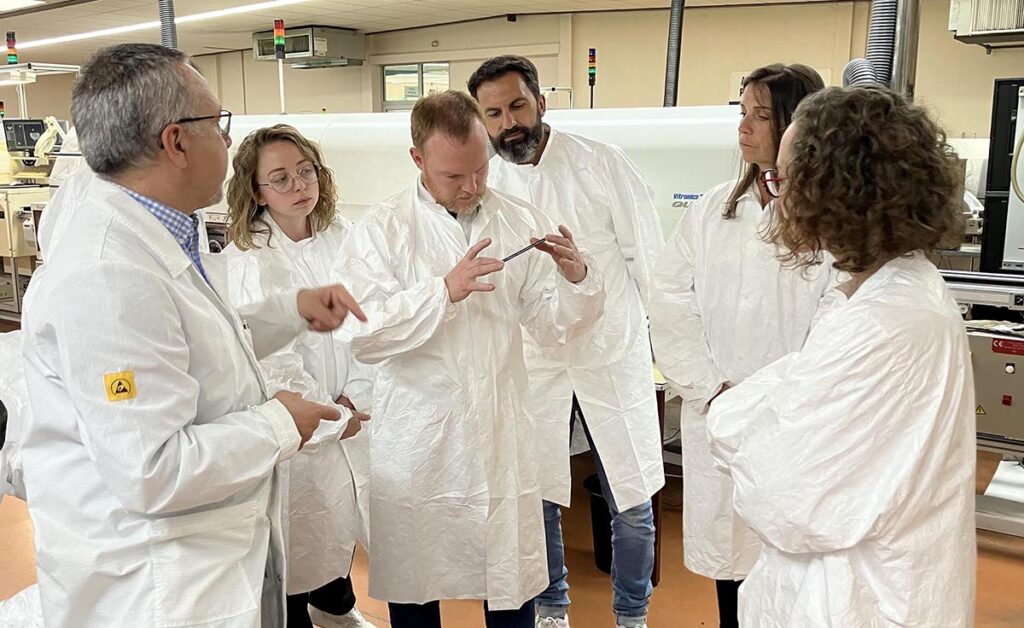 Groupe de six personnes en blouses blanches visitant l'usine SNEES, la personne au centre tient une carte électronique entre ses mains et la regarde de près.